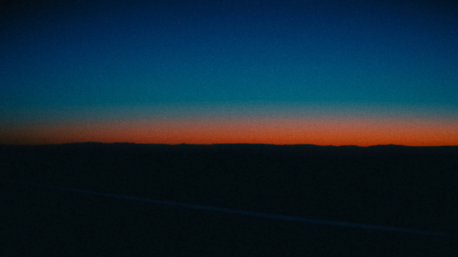 A thin orange line of sunset on the horizon, seen from a plane at dusk.